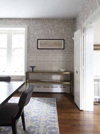 dining room with wainscoting, wallpaper above, rug, wooden floor, console table, artwork