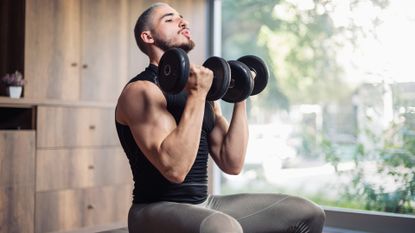 Man doing shoulder dumbbell exercises sat on a weight bench