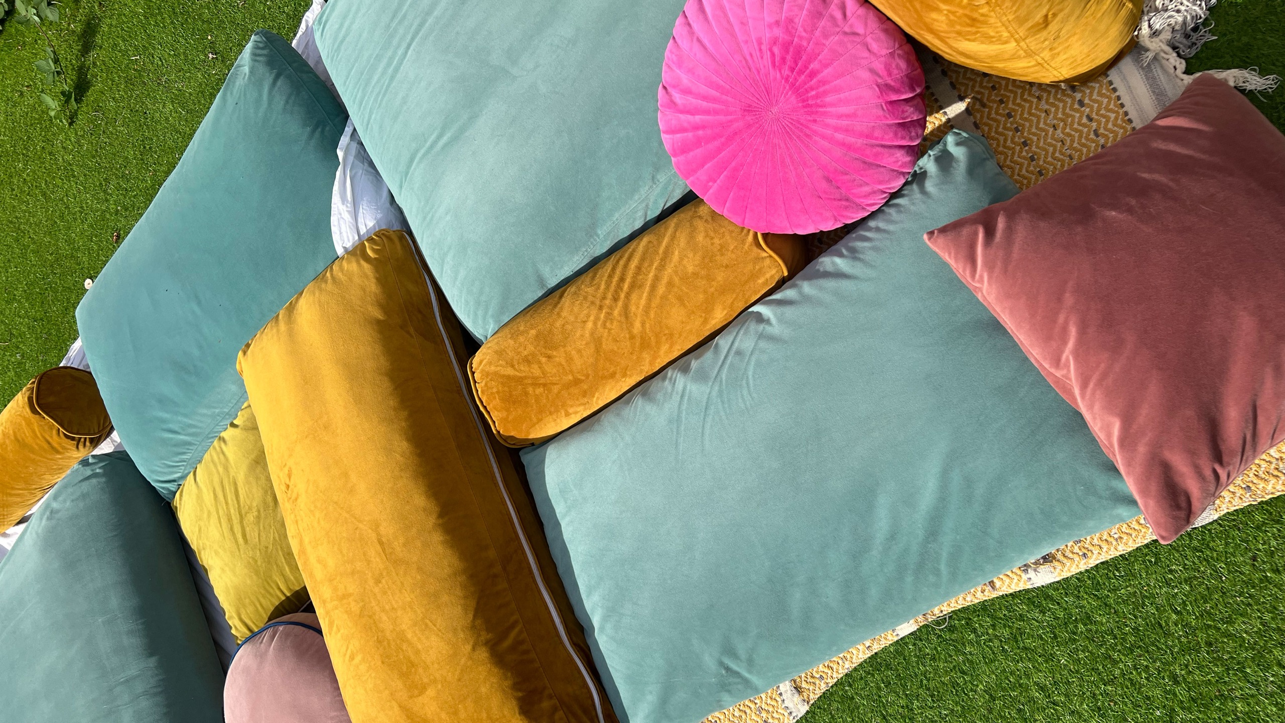 Pile of gold, teal and pink cushions on grass