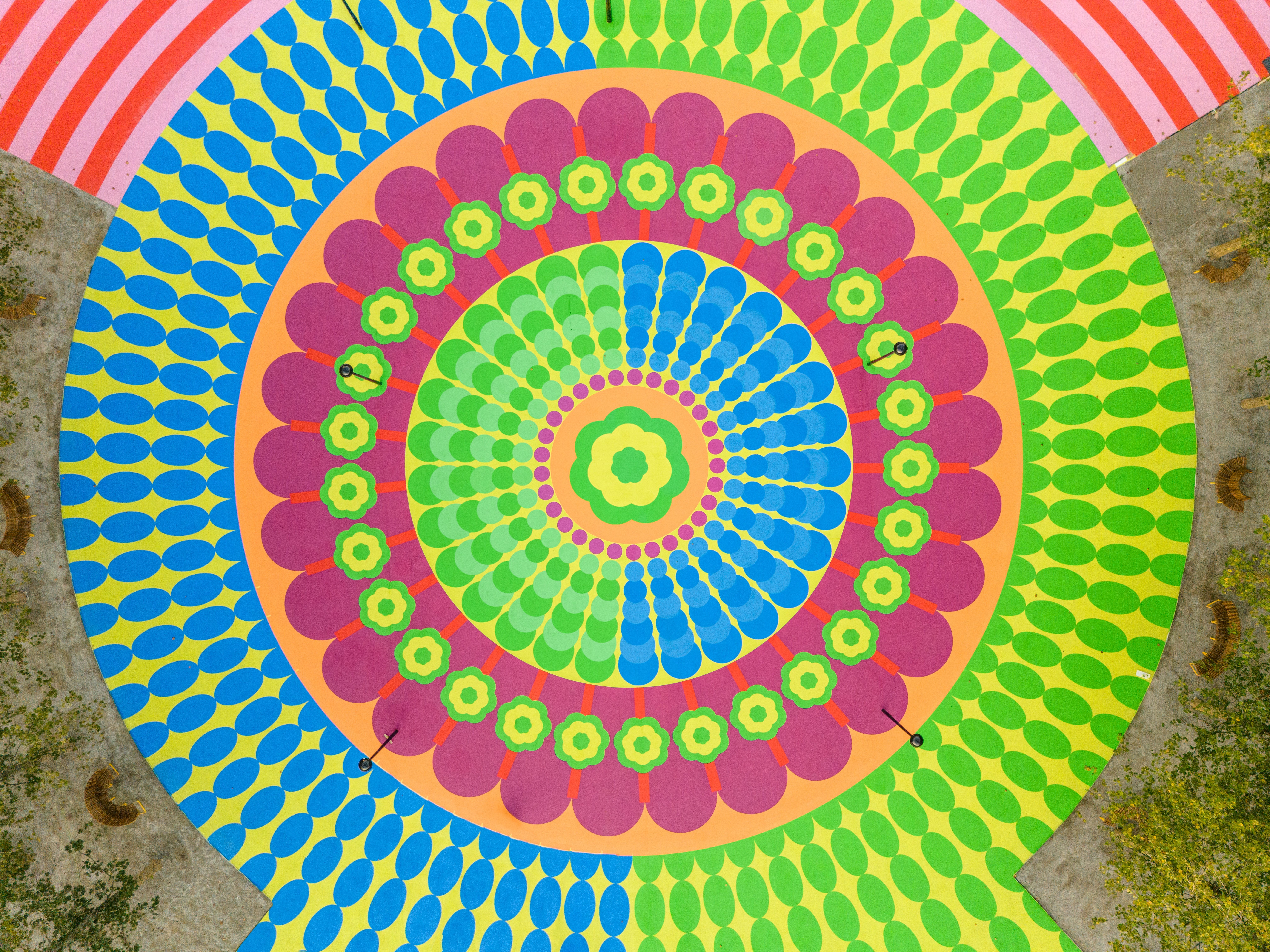 Aerial view of a colorful mural in pink, green, yellow, blue, orange, and red tones, with organic shapes resembling flower petals.