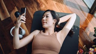 A lady uses her phone while lying on a gym mat