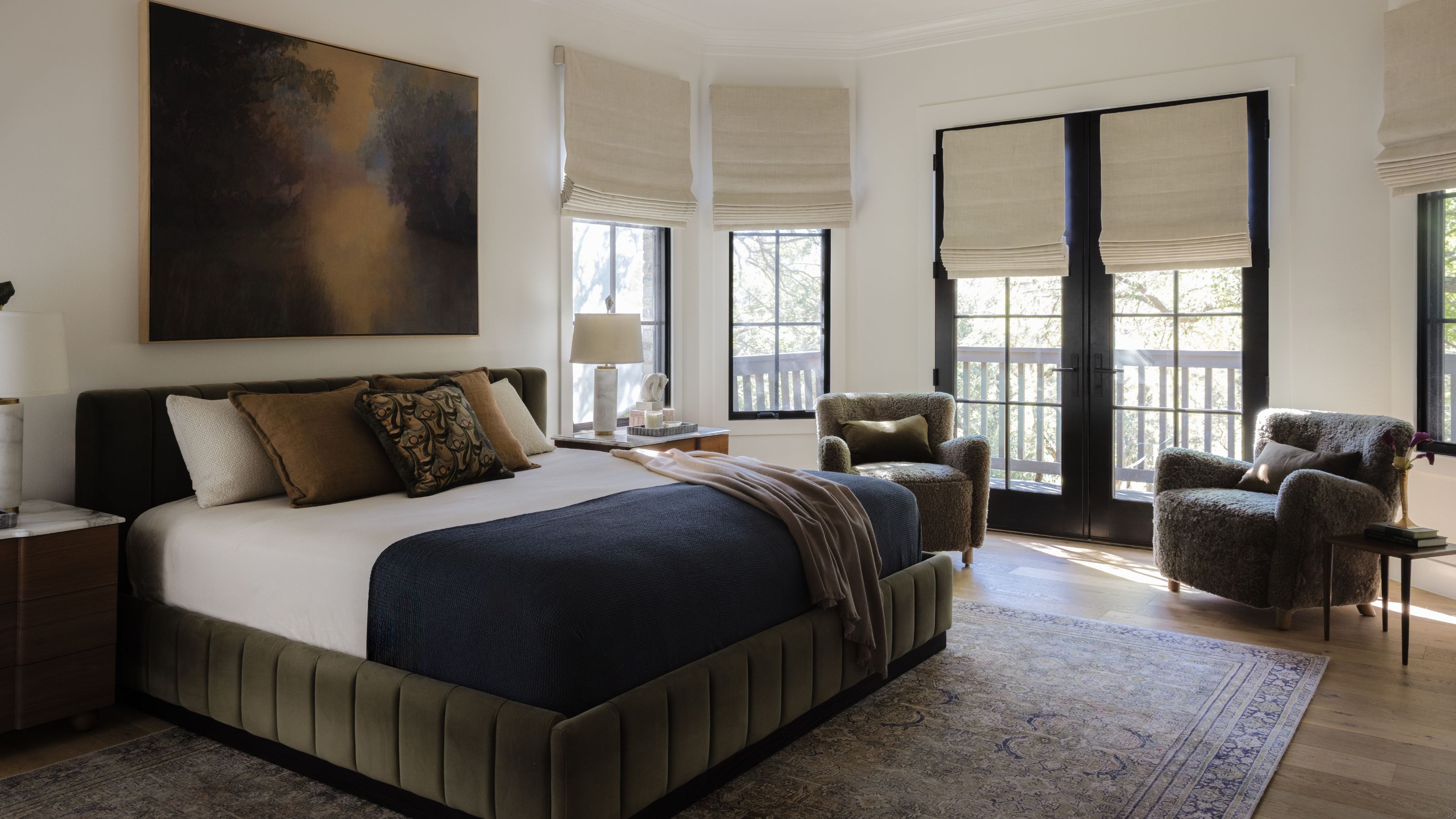 a large open primary bedroom with french patio doors, a green velvet bed, vintage rug, and seating area in front of the doors with two shearling armchairs