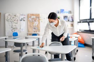 A teacher wearing a mask while cleaning a classroom.