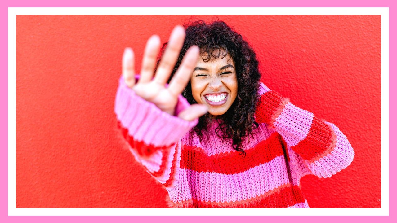 How to practice self-love this Valentine&#039;s Day. Pictured: Portrait of laughing young woman in front of red wall 