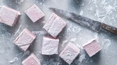 Cubes of pale pink cherry marshmallows on a cutting board with a knife