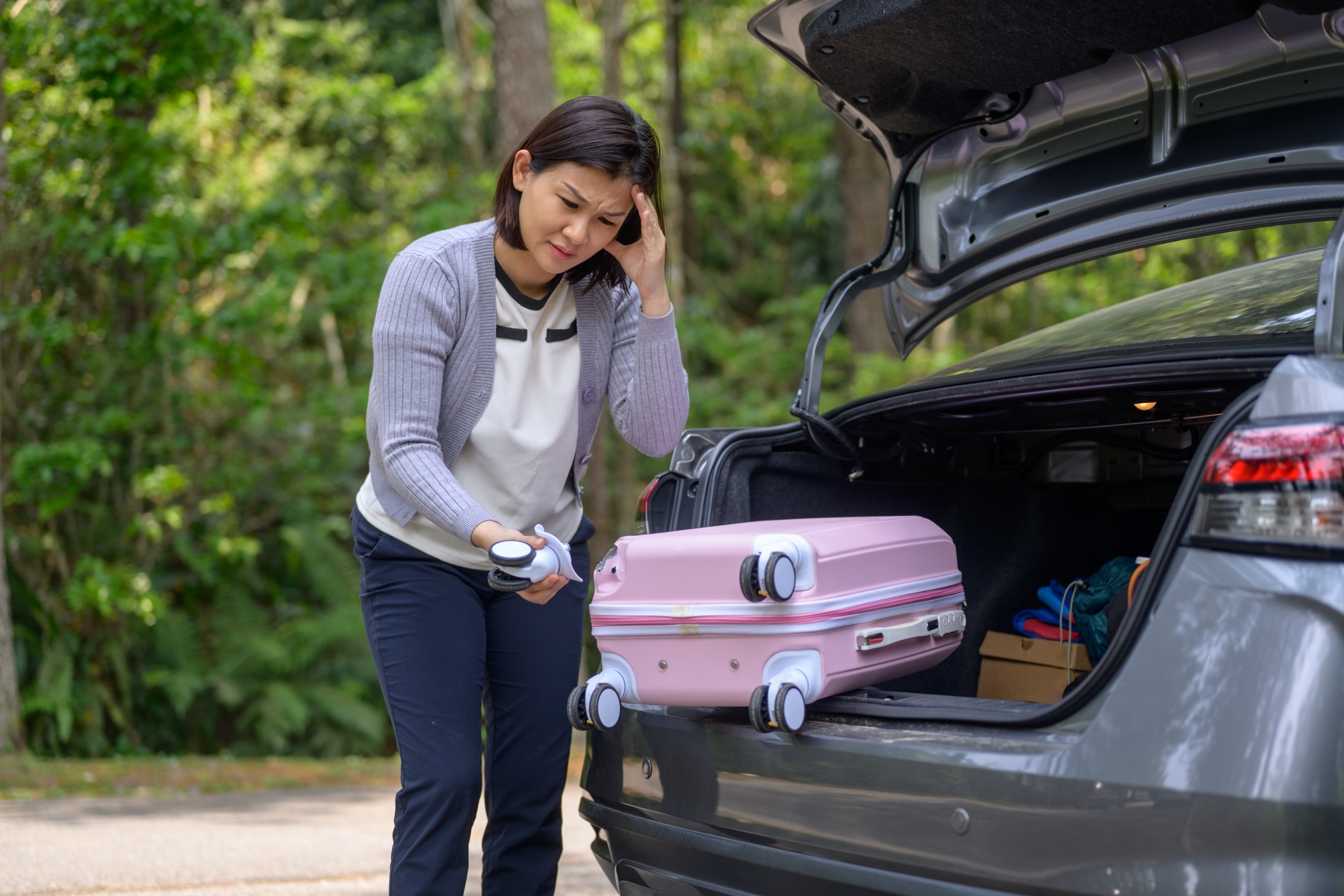 A stressed woman examines a broken wheel from her suitcase.