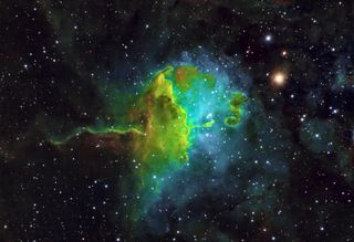the spider nebula appears as a green and blue cloud of gas and dust surrounded by stars.
