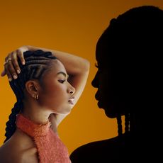 an orange background with the shadow of a woman with braids in her hair facing a black woman in a pink top with braids in her hair