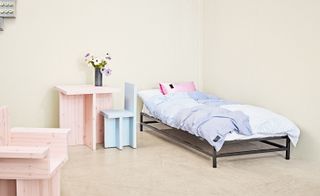 Metal-framed bed with blue striped duvet cover and pink pillowcase, alongside other bedroom furniture