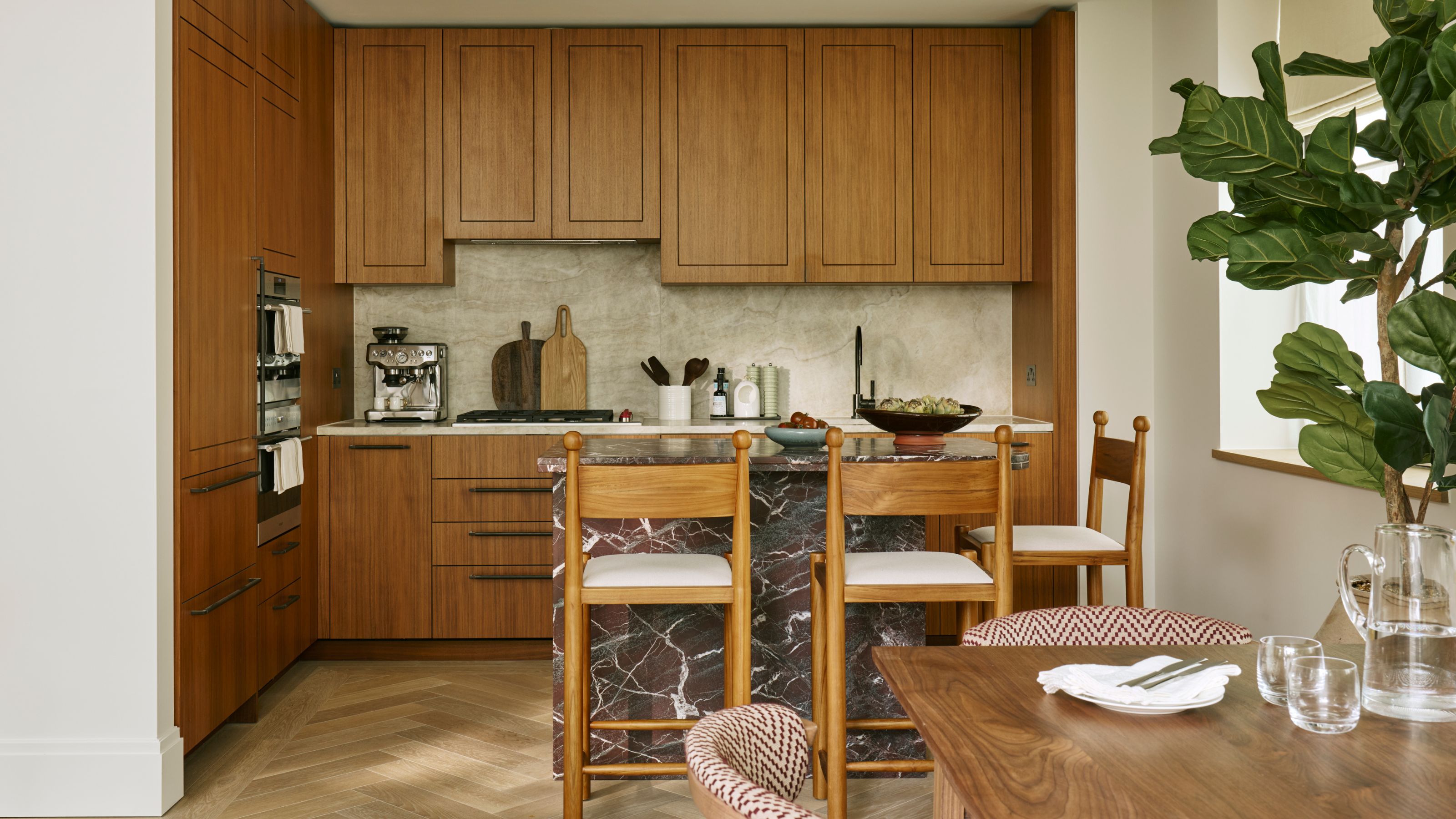 a warm oak flat paneled small kitchen with a small rosso red marble island and oak bar stools