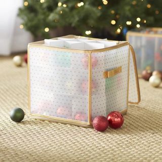 Square white flexible plastic bag with gold edges, handles and polka dot design. Pictured on cream carpet and blurred focus in background of lit festive tree