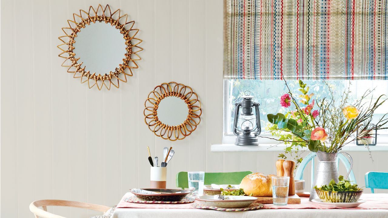 Neutral living room with tablecloth covered table, patterned window blind and two mirrors on window