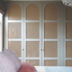 A bedroom with built-in wardrobes decorated with arched cut-outs filled with cane webbing