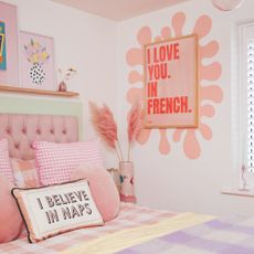 A pastel-coloured bedroom with checked bed linen, a statement cushions and art print on the wall with a wavy edge
