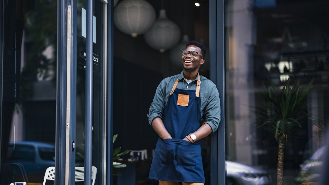 A business owner smiles as he stands outside his coffee shop.