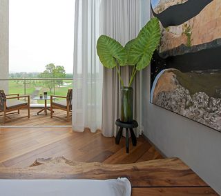 2 grey and brown chairs with a round side glass side table on a balcony with wooden floors overlooking a golf course