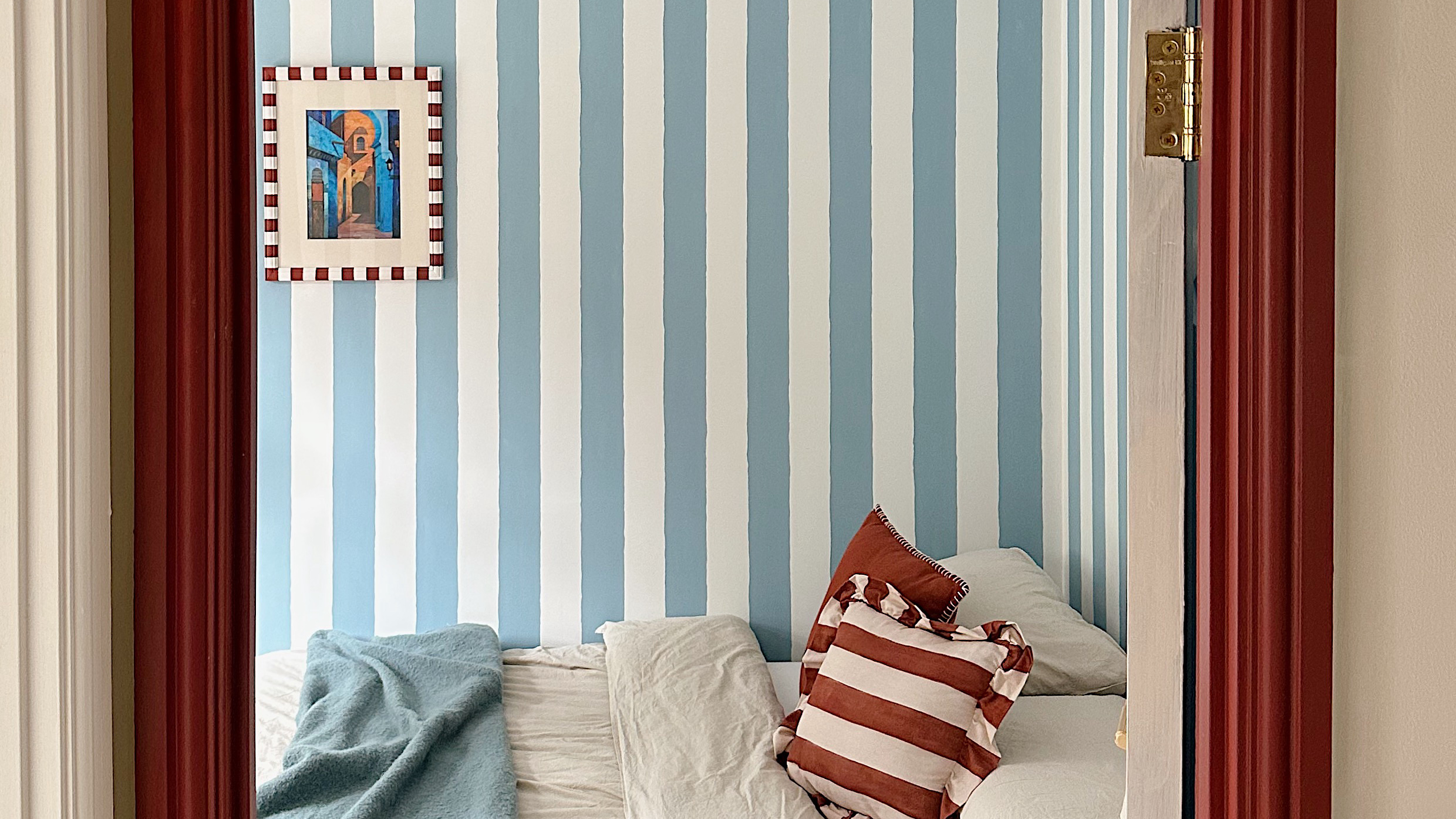 bedroom with blue and white striped wall, red woodwork and red striped cushions on the bed