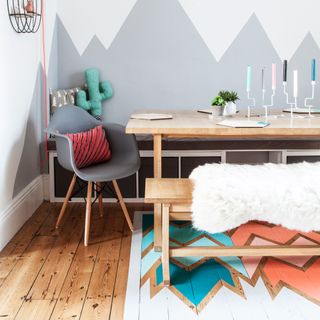 A dining area with wooden flooring, a wooden table, grey chair and grey and white mountain effect wall pattern with patterned floor