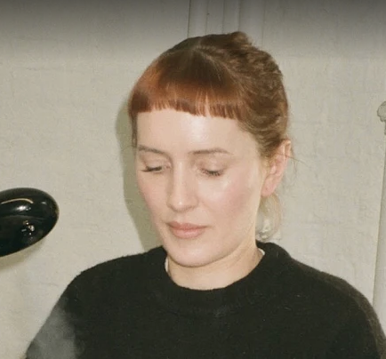 a headshot of a white woman with red bangs and a black shirt
