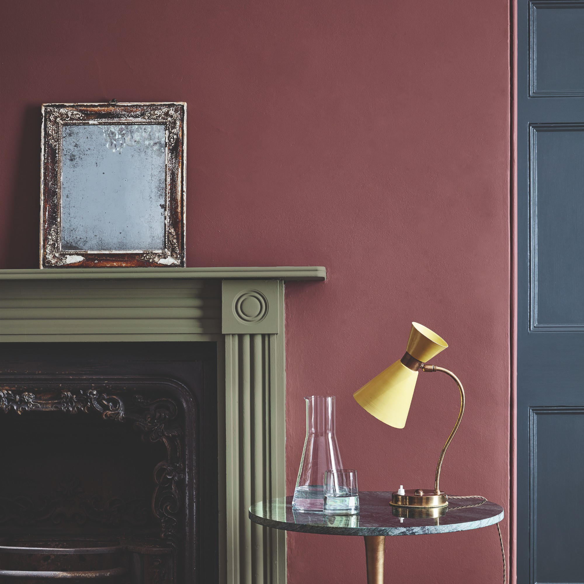 A wall painted in Little Greene&#039;s Adventurer dark red shade with a green fireplace