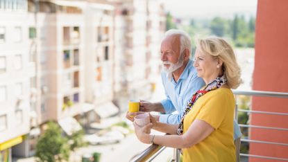 Senior couple drinking coffee on a balcony in a city.