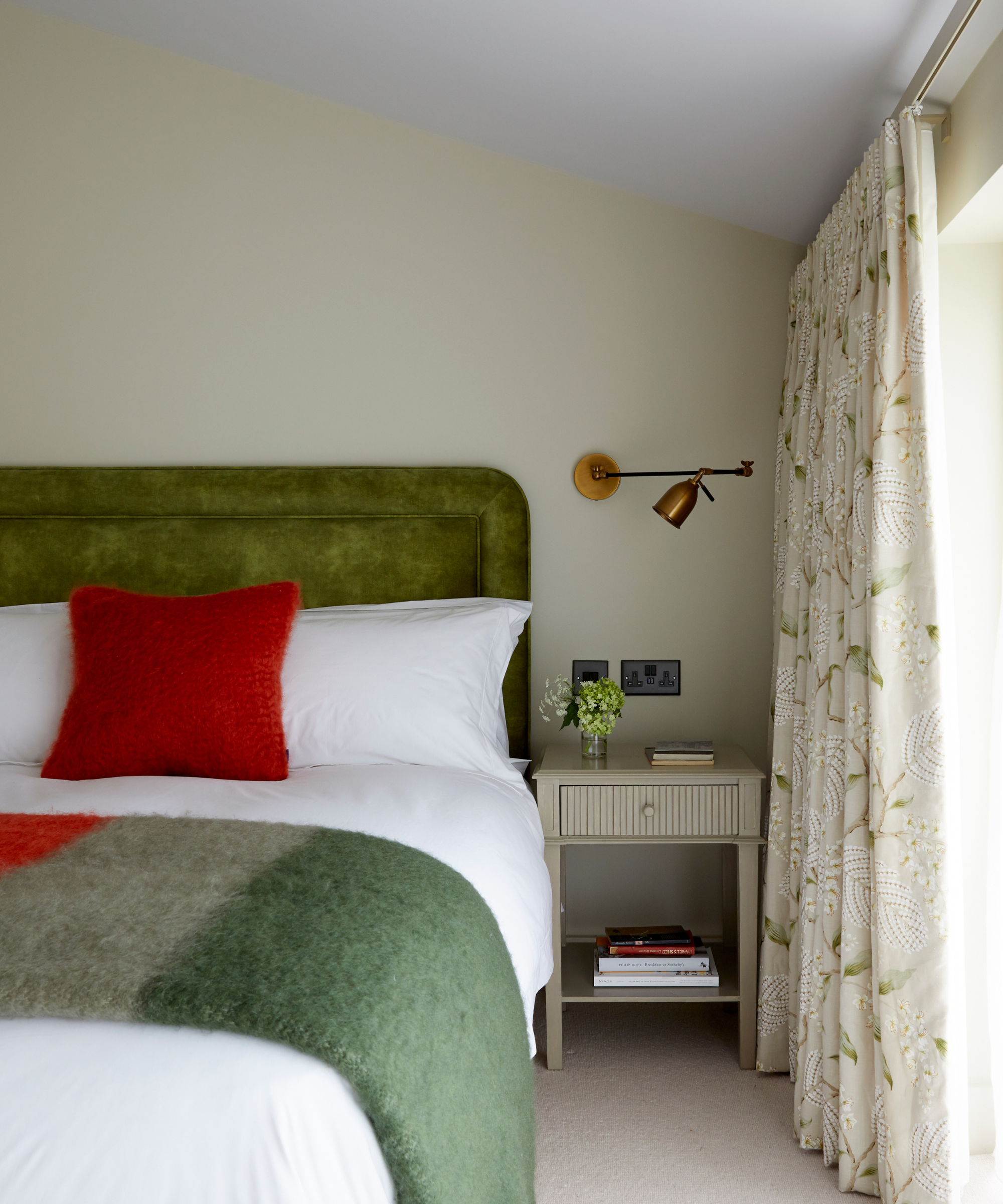 a cozy bedroom with a green headboard, white bedding, a red pillow, a green blanket, and soft green painted walls