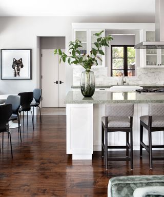 Kitchen with dark wood flooring, white and gray walls and cabinetry, kitchen island, bar seating, separate dining table
