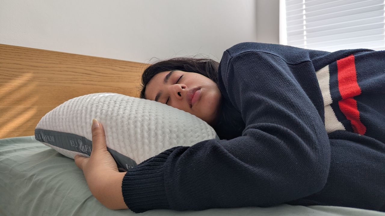 Woman sleeping on the Eli and Elm Side Sleeper Pillow in a bright lit room on the bed with a green bedsheet