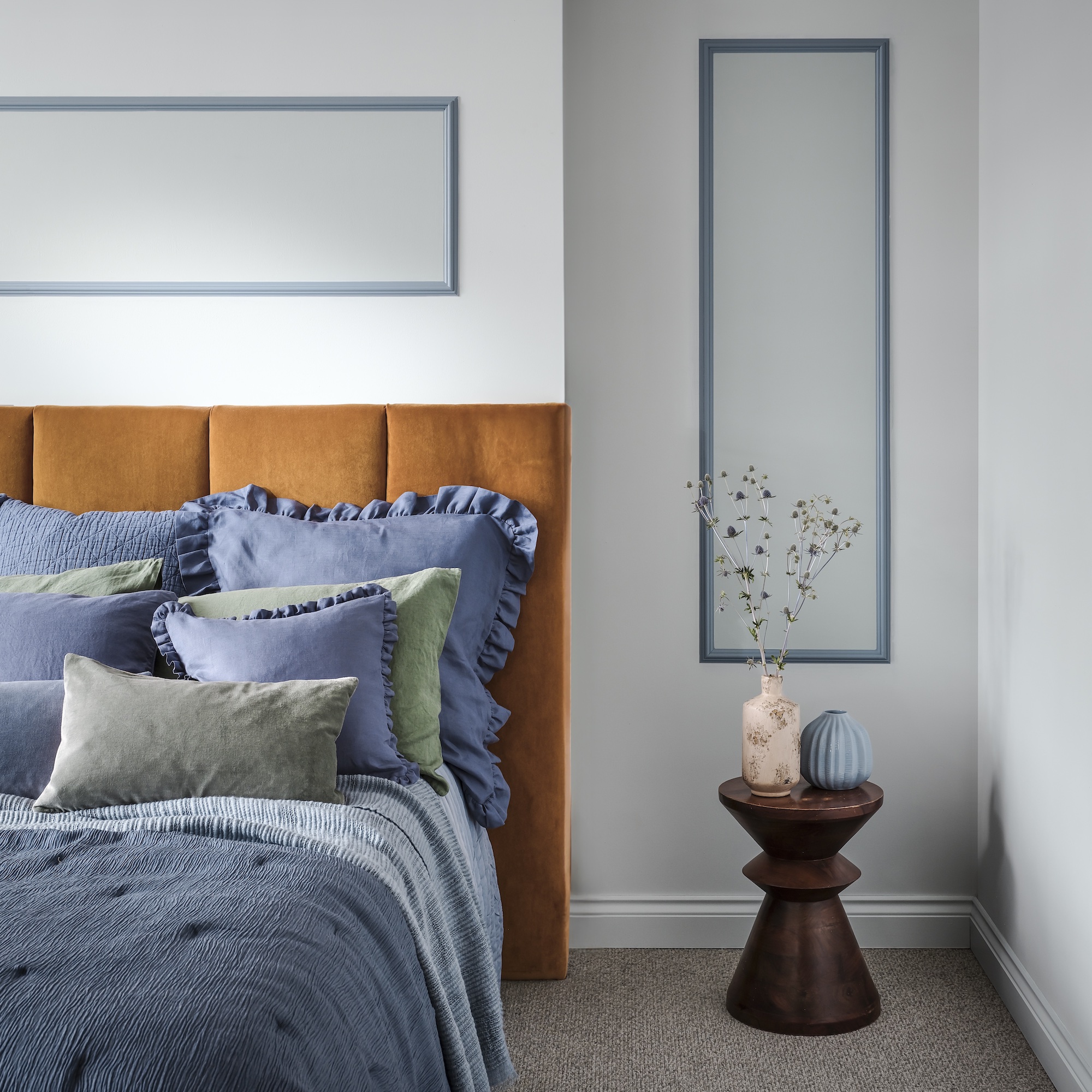 bedroom with pale blue wall and mustard headboard and denim bedding