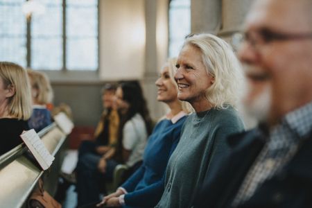An older couple and their adult daughter smile in the pews at a church service.