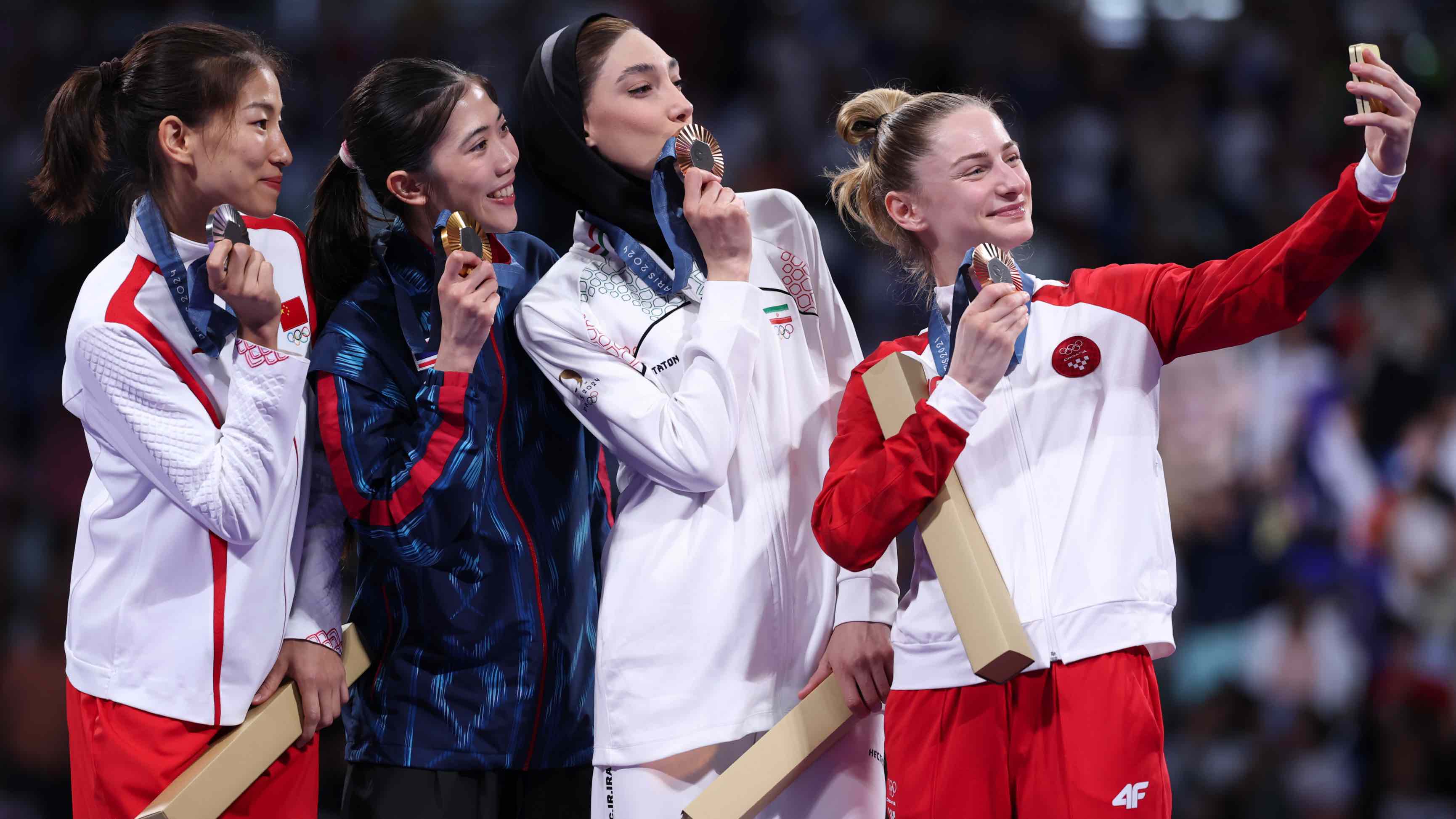 Gold medalist Panipak Wongpattanakit of Team Thailand, silver medalist Qing Guo of Team People's Republic of China, bronze medalist Lena Stojkovic of Team Croatia and bronze medalist Mobina Nematzadeh of Team Islamic Republic of Iran take a winner's selfie with the Samsung Galaxy Z Flip6 Olympic Edition on the podium during the medal ceremony in the women's taekwondo -49kg on day twelfth of the Paris 2024 Olympic Games at the Grand Palais on August 07, 2024 in France. (Photo by Alex Pantling/Getty Images)