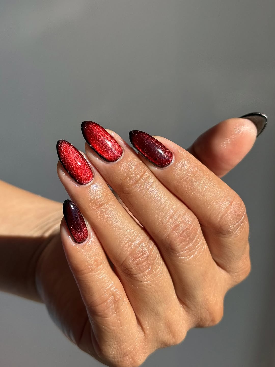 Close-up photo of a person&amp;rsquo;s hand showcasing a shimmery red and black manicure on almond nails.