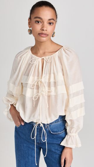 a model wears a loose-fitting white long-sleeve blouse with jeans