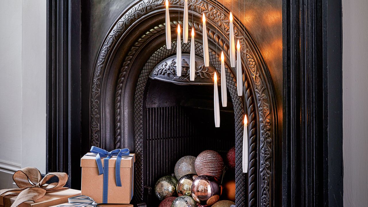 Black fireplace with floating candles hanging at various heights in front of the opening and baubles stacked in the fireplace