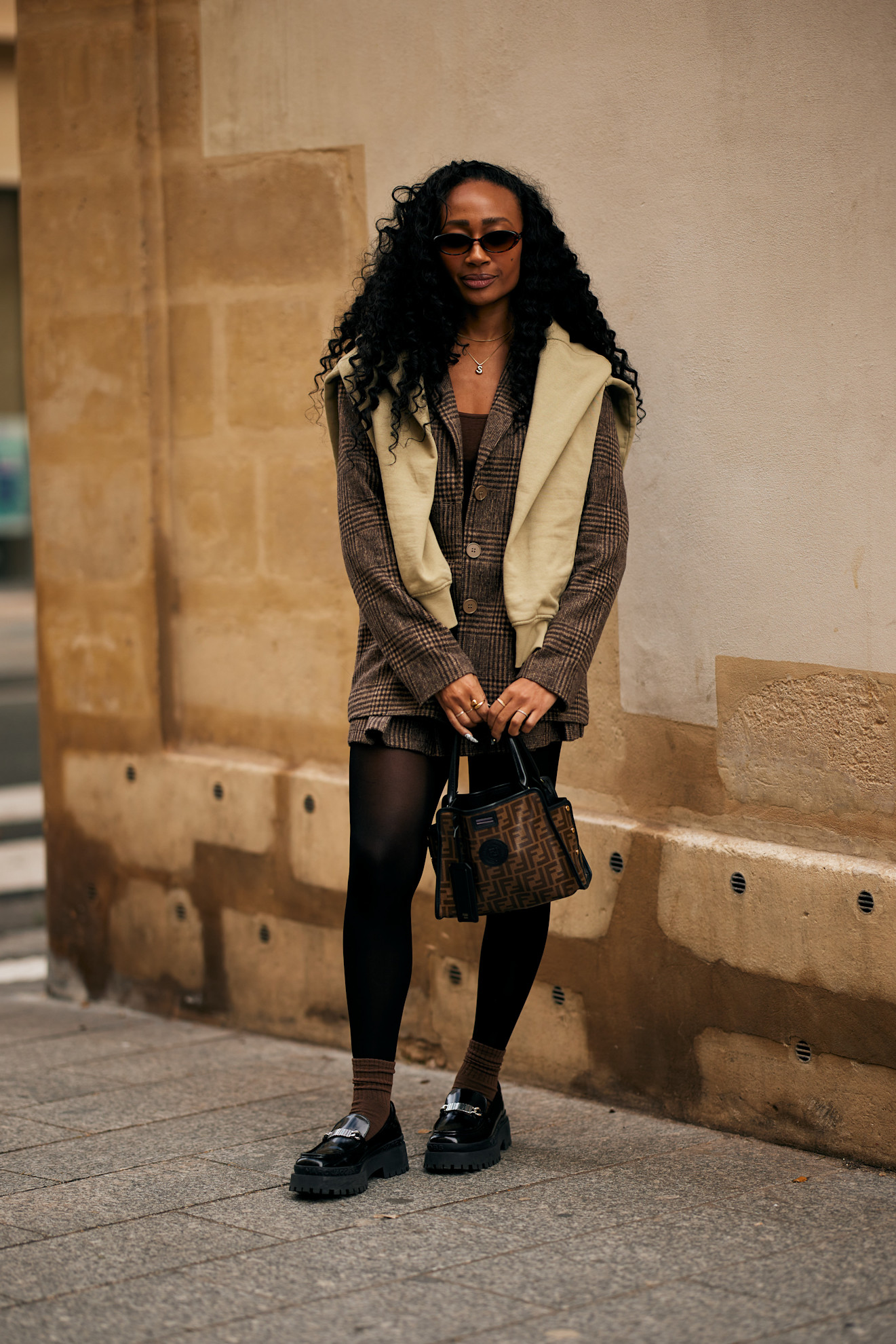 woman wearing black loafers, brown checked blazer, skirt, and yellow sweater