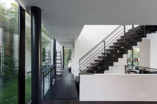 Interior view of the two-floor, all-glass villa. White walls, with black columns, dark wood floors, and stairs.
