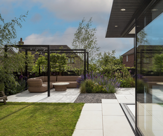Garden with a patch of grass, pergola seating area, and patio with glass box extension just in view in right corner