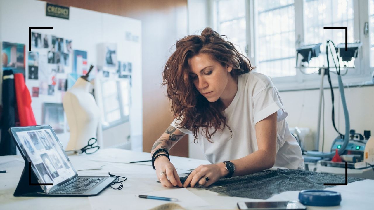 woman cutting fabric looking at photographs on tablet