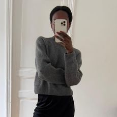 Woman wearing grey cashmere sweater and black pencil skirt, taking mirror selfie.