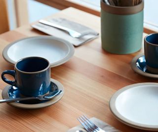 Heath Ceramics mug on a wooden table with plates and cutlery