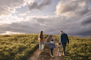 A happy family enjoying a walk together in a field on a cloudy yet sunny day.