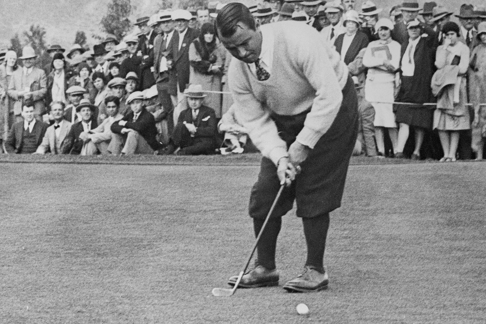 Gene Sarazen holing a putt on the green in front of a crowd of spectators