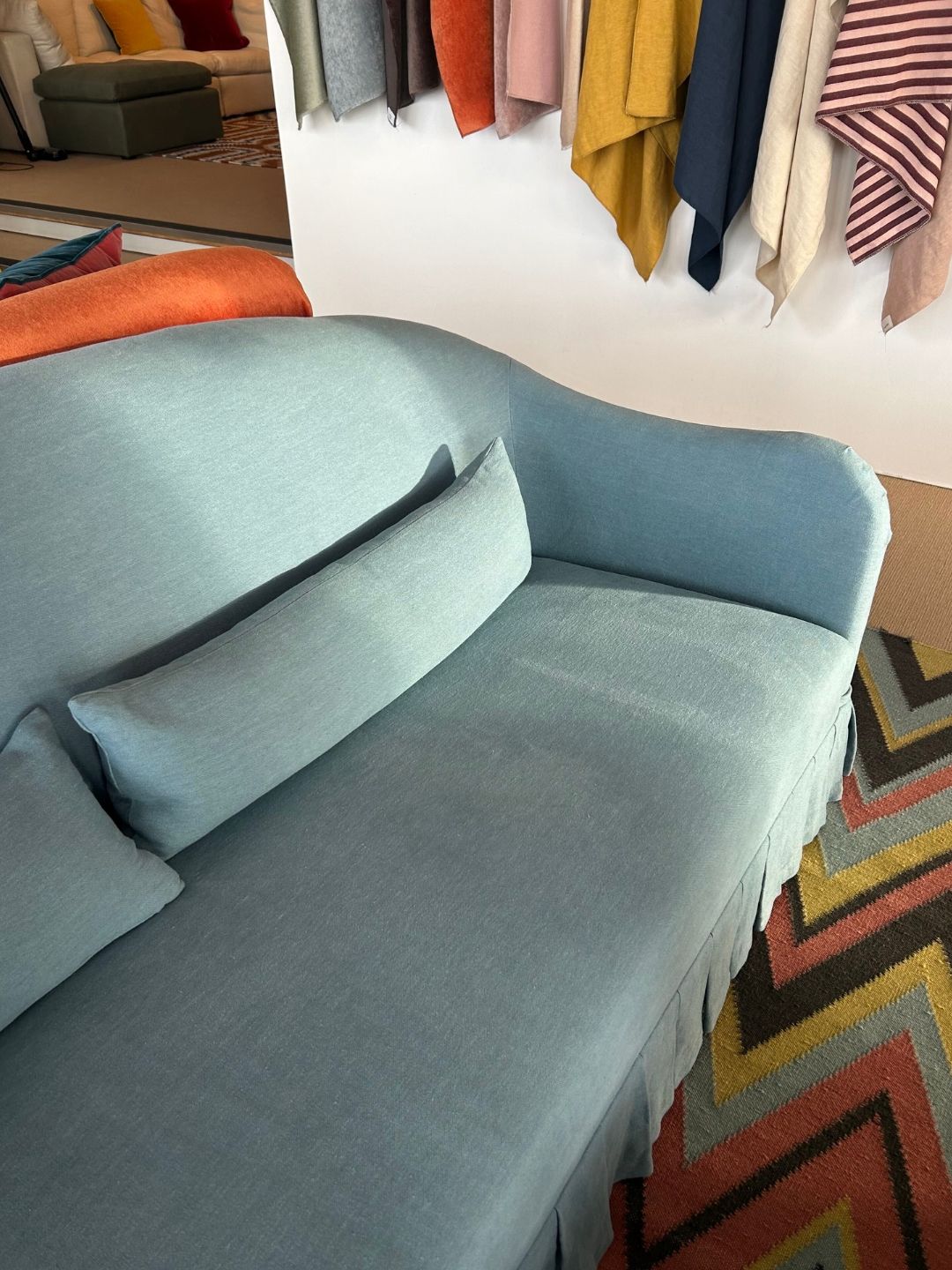 Close-up of the Edie sofa in pale Skye linen, showing its continuous sprung seat, curved backrest and matching bolster cushions.
