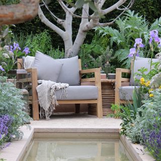 Wooden outdoor armchair with grey cushions on the edge of a modern garden pond