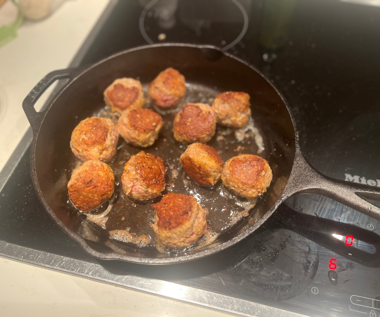 Meatballs frying in a black cast iron skillet on an electric stovetop
