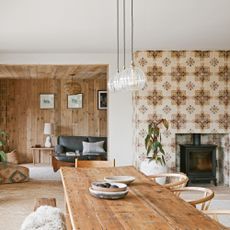 living dining space with an entrance to a snug room in the background, with a floor-t-ceiling tiled chimney breast with woodburner and dining table and chairs