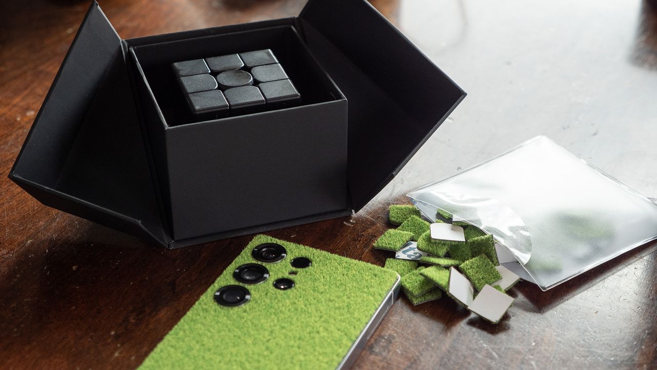 The Touch Grass DBrand skin on a Samsung Galaxy S25 Ultra alongside a DBrand Rubix Cube-like toy