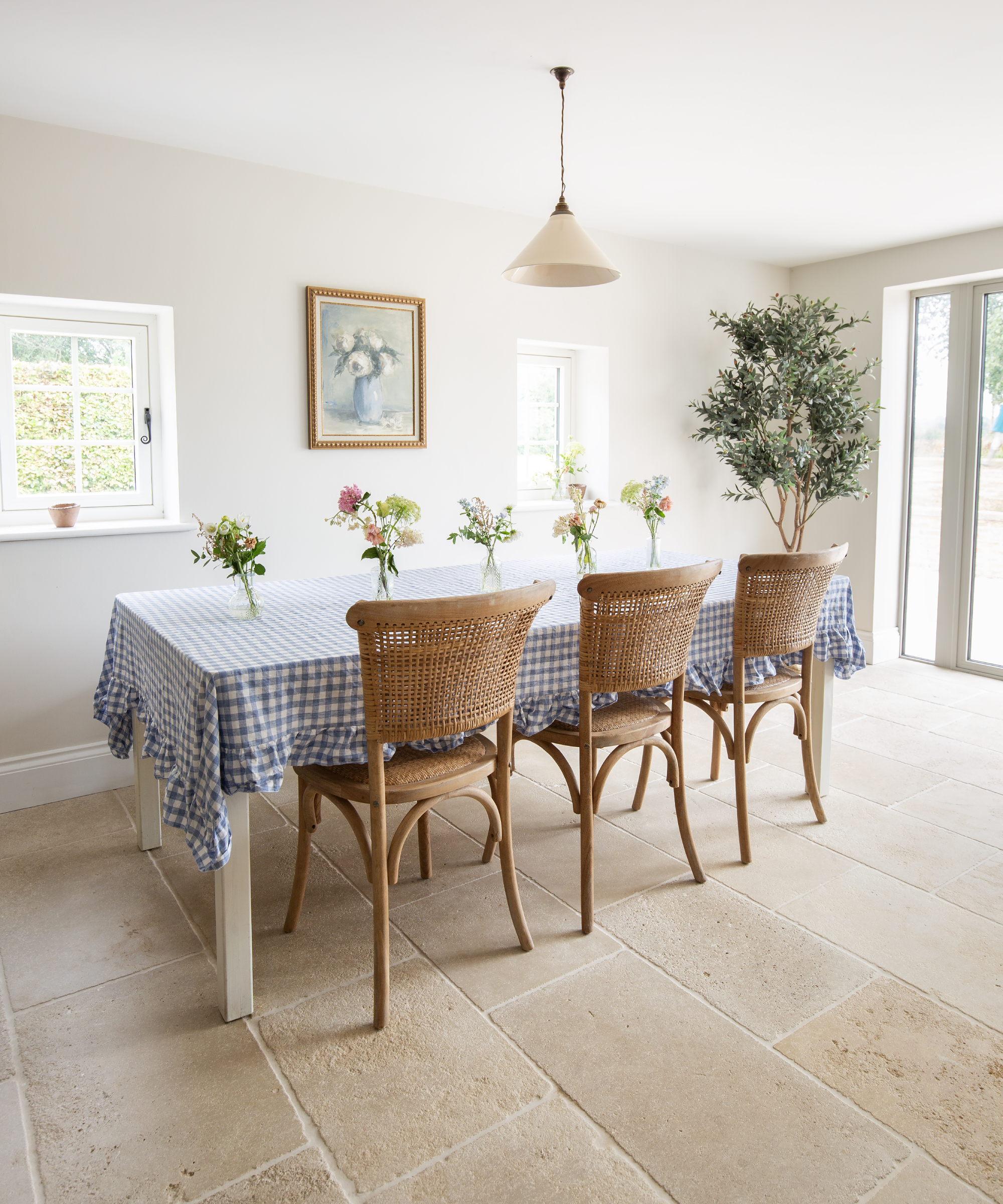 dining table with light stone slabbed floor, table with blue and white gingham tablecloth and wicker chairs