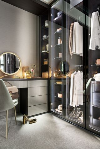 walk in closet with dressing table and chair, grey walls, glass doors lit up