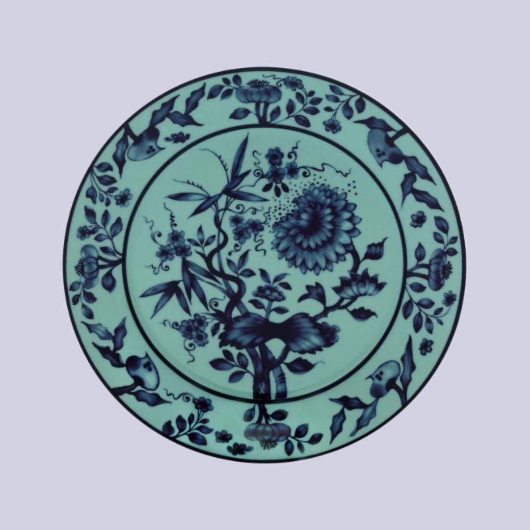 A water green porcelain plate with floral motifs in blue sits against a pale purple background.